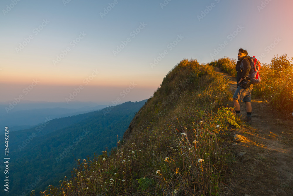 Hipster young man with backpack enjoying sunset on peak mountain. Tourist traveler on background valley landscape view mockup.