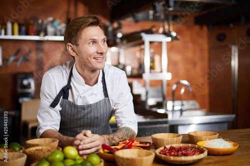 Waist up portrit of handsome chef posing in kitchen at table with spices looking away pensively  copy space