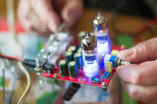 Close up old tube amplifier in male hands. Process of testing music detail with voltmeter. Illuminated lamps sound plate