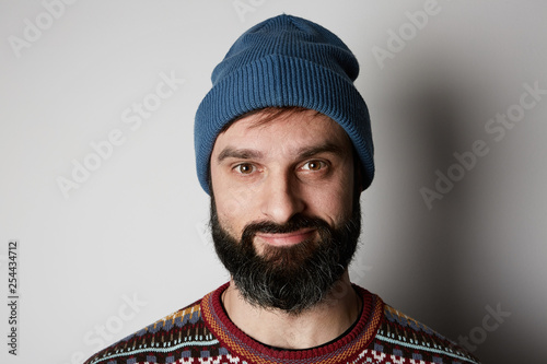 Bearded hipster wearing blue beanie and colored sweater on white background.