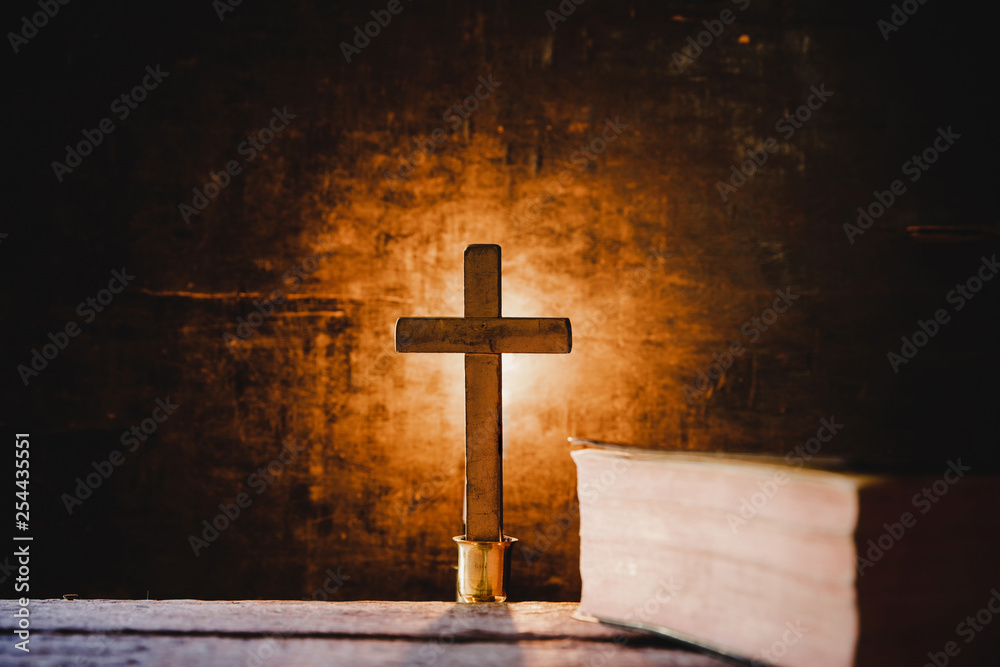 Cross with bible and candle on a old oak wooden table. Beautiful gold background. Religion concept.