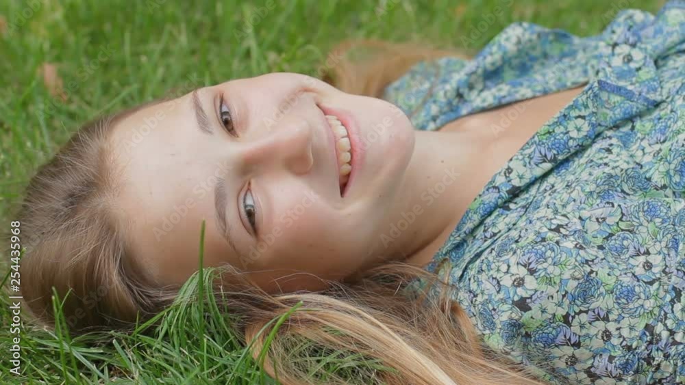 Portrait of teen girl lying on green grass smiling at camera. Happy young woman enjoying nature while resting at the park Portrait of teen girl lying on green grass smiling at camera. Happy young woman enjoying nature while resting at the park