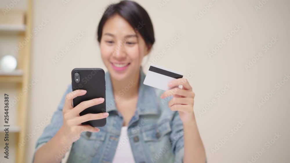 Beautiful Asian woman using smartphone buying online shopping by credit card while wear casual sitting on desk in living room at home. Lifestyle women working at home concept. Beautiful Asian woman using smartphone buying online shopping by credit card while wear casual sitting on desk in living room at home. Lifestyle women working at home concept.