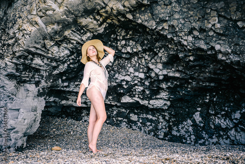 A young girl in a straw hat  hid in a cave  resting on the coast of the ocean. The concept of rest on the rocky coast.