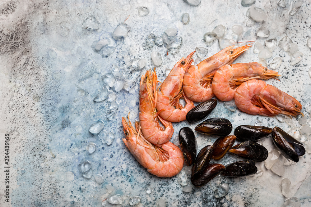 Sea food composition, flat lay of raw shrimps and mussels with ice over blue background, top view, copy space