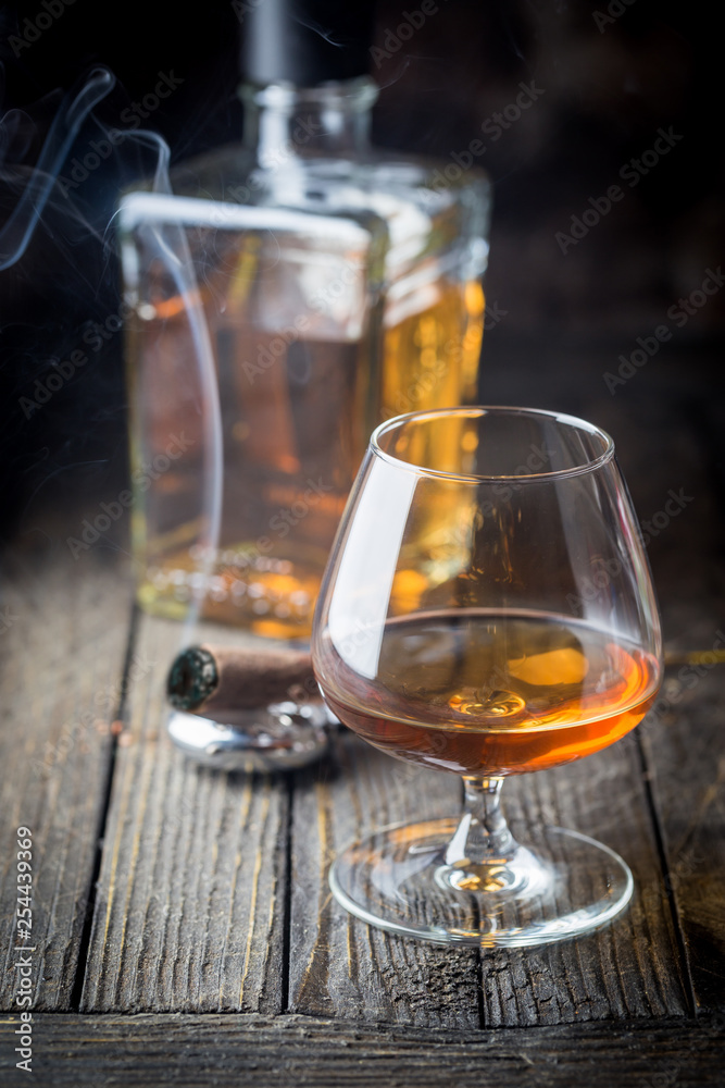 Glass and a bottle of brandy or cognac and smoking cigar on the wooden table. Glass and a bottle of brandy or cognac and smoking cigar on the wooden table.