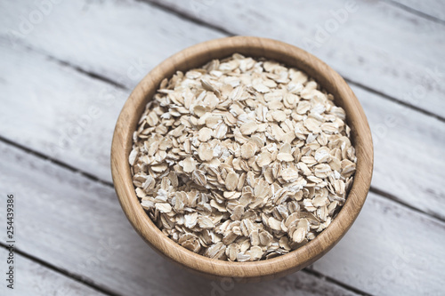 Uncooked oatmeal or oat flakes in a wooden bowl on a white wooden background