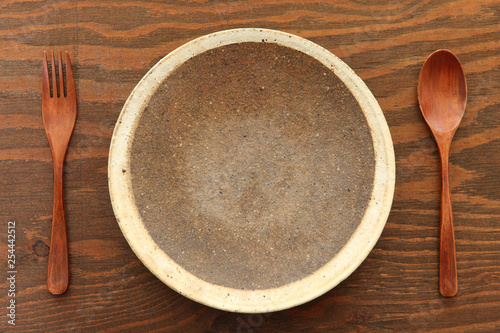  empty clay dish with wooden cutlery on the brown table