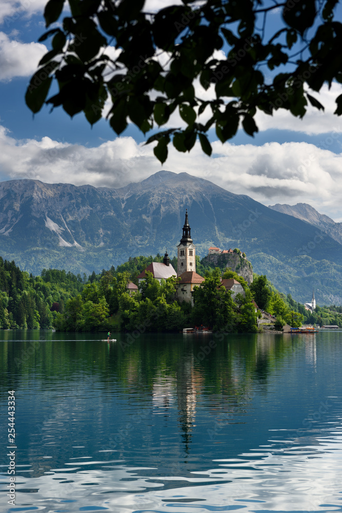 Paddleboarder on Lake Bled with Assumption of Mary church on Bled Island and St Martin church and Veliki Stol peak Karawanks mountain Slovenia