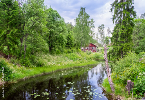 Idyllic river with old abandoned cottage and green lush trees at summer day in Finland