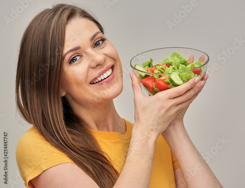 smiling woman holding glass bowl with green salad.