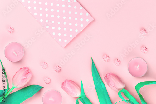 Tender feminine pastel pink green tulip flowers dotted envelope with candles and sweets on trendy pinky background. Flat lay with copy space for blogger with spring, gift and celebration concept