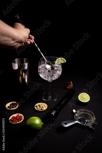 barman preparing a gin and tonic cocktail on a black background next to his ingredients
