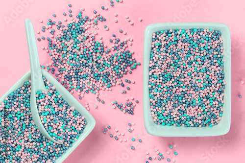 Colorful nonpareils cake candy sprinkles in two white rectangular bowls and spoon on pink background in flat lay with copy space. Party celebration or bakery concept photo