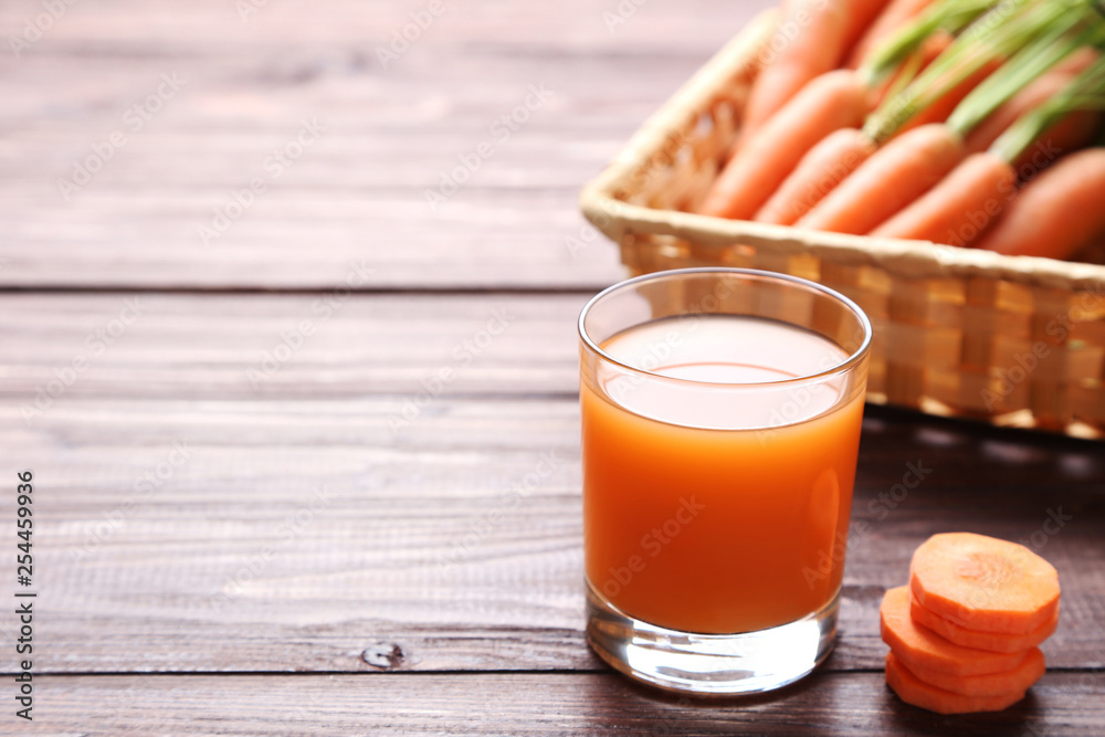 Fresh carrot with glass of juice on wooden table
