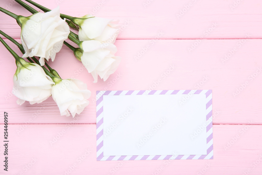 Greeting card with eustoma flowers on pink wooden table