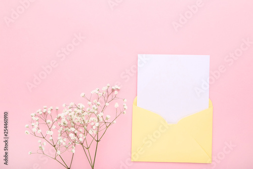 Blank paper with envelope and gypsophila flowers on pink background