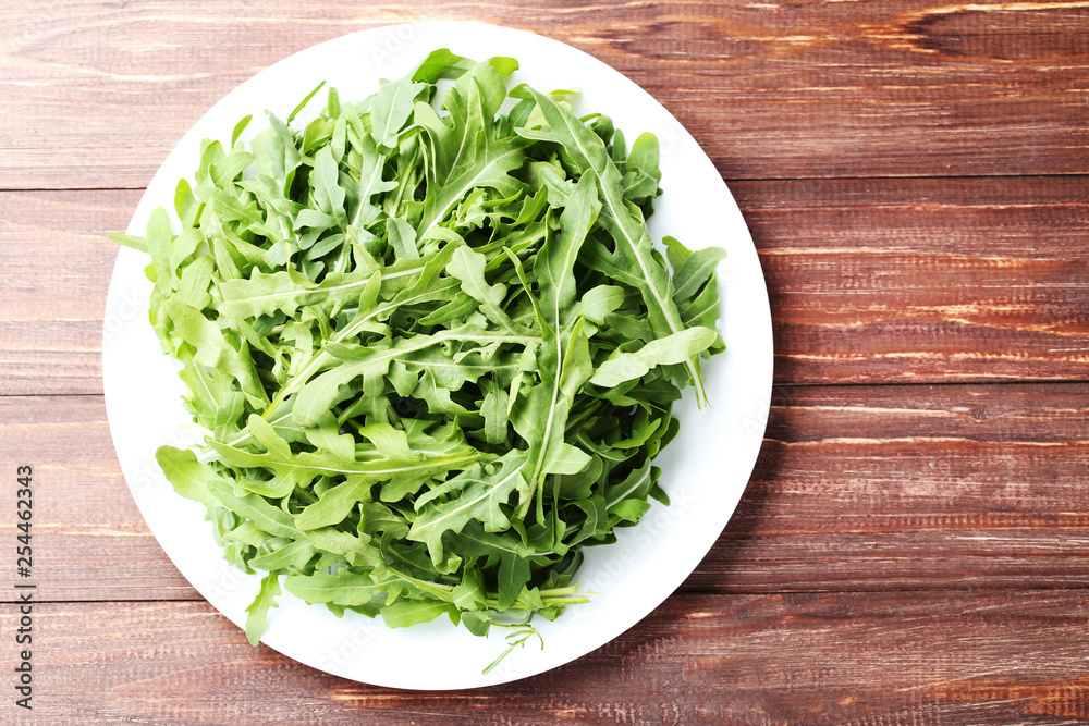 Green arugula leafs in plate on brown wooden table Green arugula leafs in plate on brown wooden table