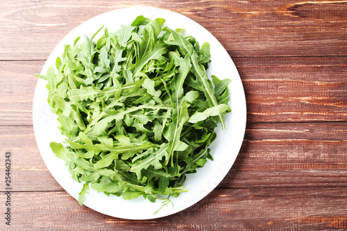 Green arugula leafs in plate on brown wooden table