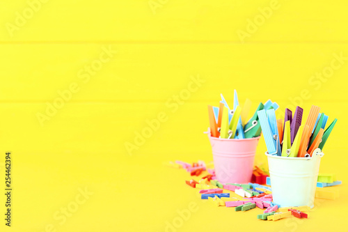 Colorful plastic clothespins in buckets on yellow background