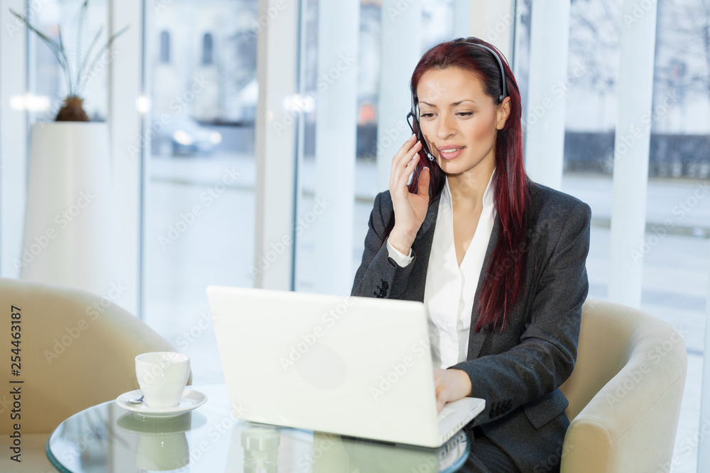 Woman with headphone talking and using a laptop computer Woman with headphone talking and using a laptop computer