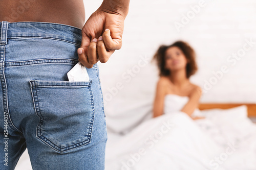 Fotografie Man taking condom from jeans, woman waiting in bed