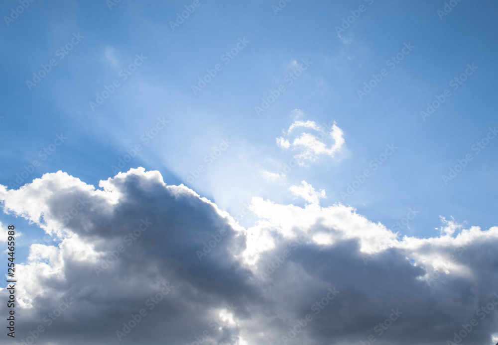 Obraz premium Sunbeam, white and dark cumulus clouds in the blue sky.