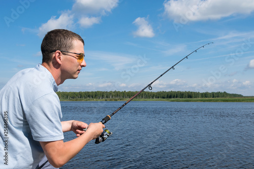 side view, a man with glasses is fishing for spinning in open water