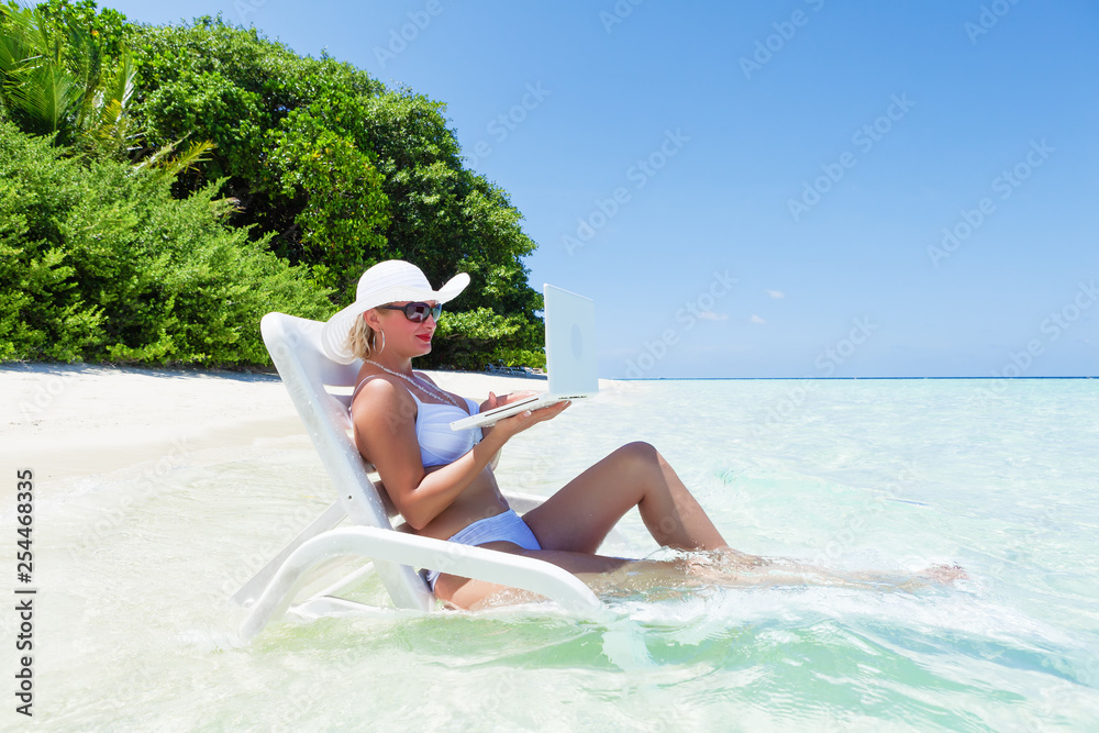 young woman relaxing on the beach, using laptop