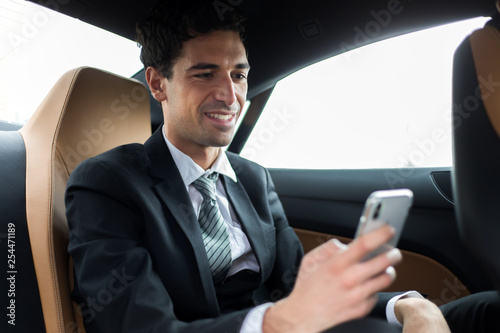 Handsome man with phone sitting in the backseat of a car © Minerva Studio