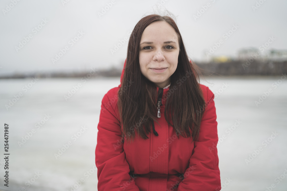 Beautiful girl in a red jacket on the pier in the spring posing against the water. Woman on the waterfront Beautiful girl in a red jacket on the pier in the spring posing against the water. Woman on the waterfront