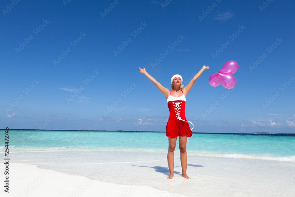 Santa Claus woman standing at the beautiful white sand beach and holding the Christmas pink balloons. Copy space