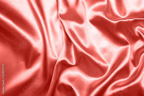 Close up of ripples on silk fabric. Satin textile background. Living Coral color. Top view. Color of the year 2019.