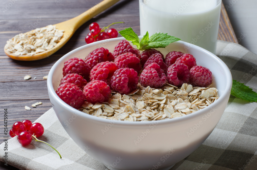Healthy vegetarian food. Oatmeal with raspberry. Wooden spoon with cereals, milk in a glass, red currant. Brown wooden background. Healthy vegetarian food. Oatmeal with raspberry. Wooden spoon with cereals, milk in a glass, red currant. Brown wooden background.