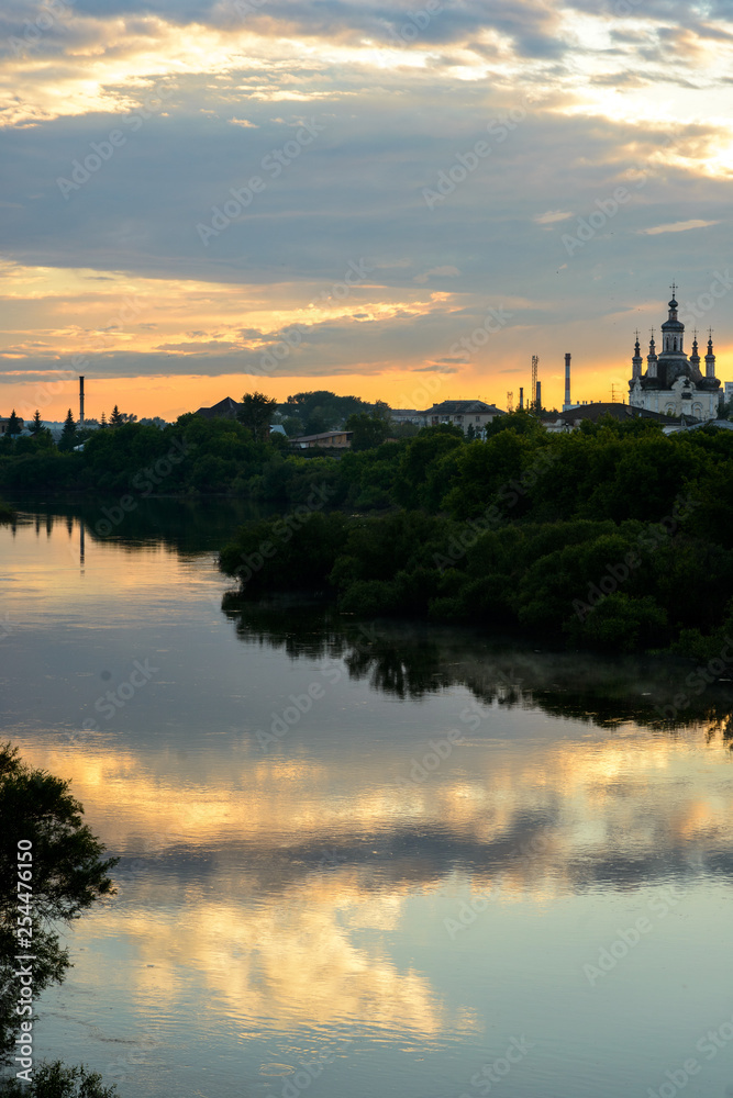 landscape of mirror river and small russian church with  amazing sunset on background in village area.