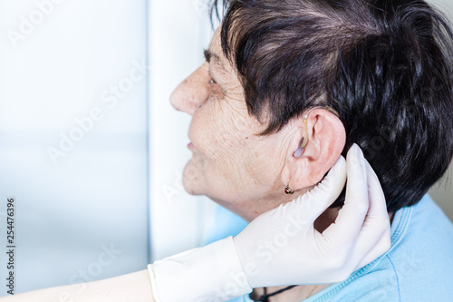 Female doctor putting a hearing aid in to the senior woman's ear 