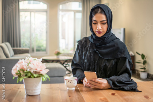 Photography Beautiful muslim woman wearing abaya using smart phone while sitting at her luxury apartment