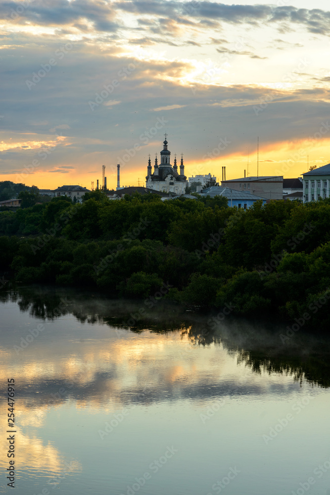 landscape of mirror river and small russian church with  amazing sunset on background in village area.