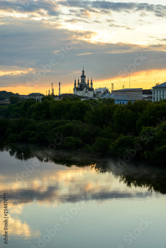 landscape of mirror river and small russian church with amazing sunset on background in village area.
