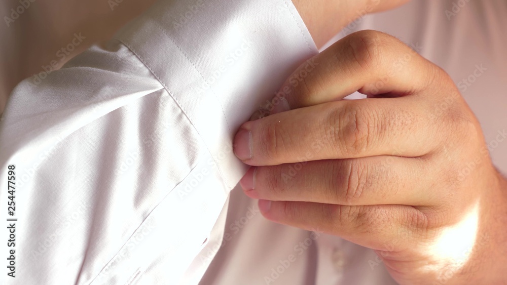 office worker gets dressed in the morning. businessman puts on white shirt. men fastens a button on shirt. close-up. a man gets dressed for work .