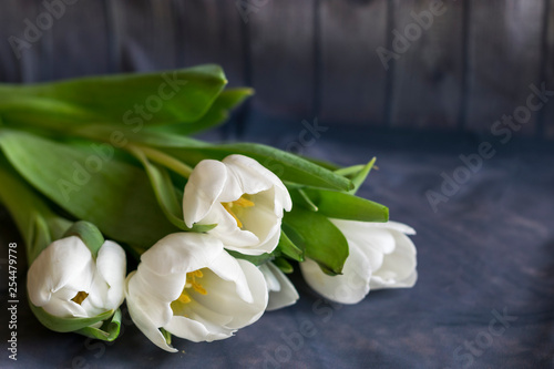 A bouquet of white tulips is on the table , the background is wooden.