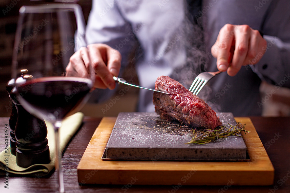 sirloin steak on a very hot stone being cooked by a man to his own taste on a wooden table with a knife and fork sirloin steak on a very hot stone being cooked by a man to his own taste on a wooden table with a knife and fork