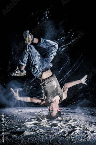cool dirty vietnamese  guy dancer in style of bboying doing complex tricks on floor in Studio filled with flour on black background. concept of space dance on surface of planet moon