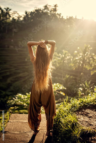 beautiful woman with long red hair in casual clothes posing back by rice terraces in Bali