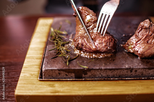 sirloin steak on a very hot stone being cooked by a man to his own taste on a wooden table with a knife and fork