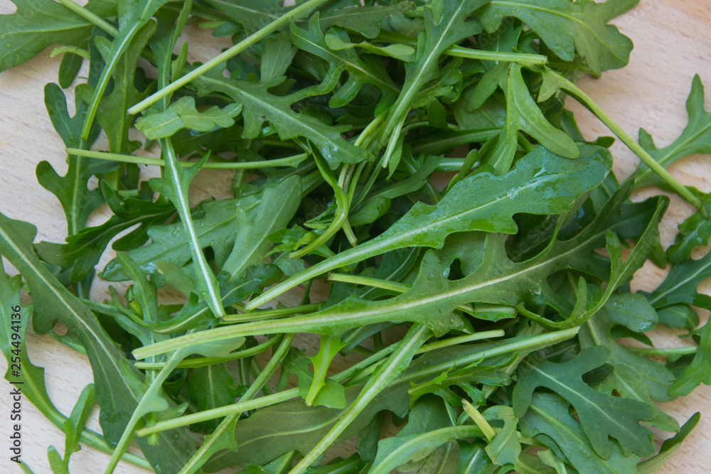 Green arugula leaves on wooden cutting board. Fresh rucola in the kitchen in plastic tray, Italian seasoning. Healthy lifestyle organic food Green arugula leaves on wooden cutting board. Fresh rucola in the kitchen in plastic tray, Italian seasoning. Healthy lifestyle organic food