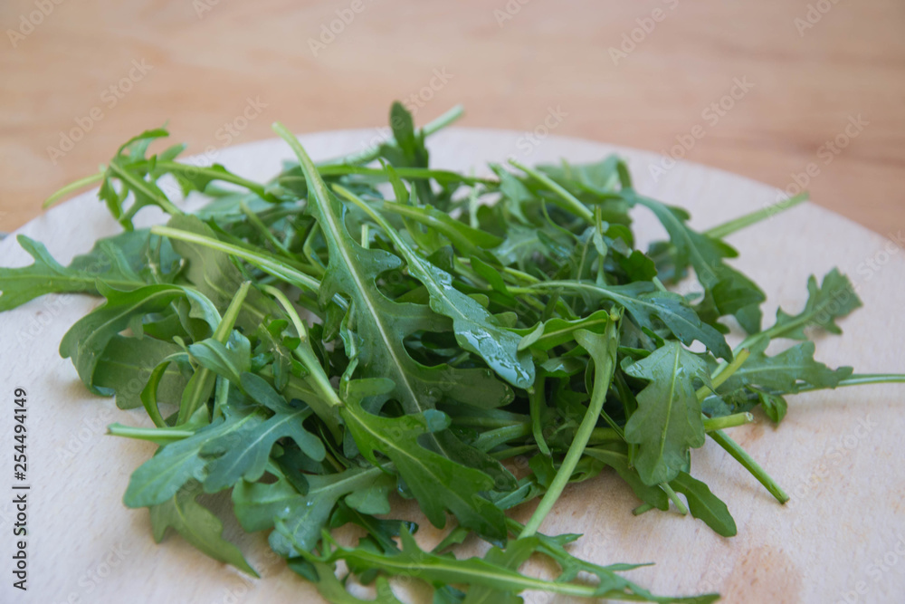 Green arugula leaves on wooden cutting board. Fresh rucola in the kitchen in plastic tray, Italian seasoning. Healthy lifestyle organic food Green arugula leaves on wooden cutting board. Fresh rucola in the kitchen in plastic tray, Italian seasoning. Healthy lifestyle organic food