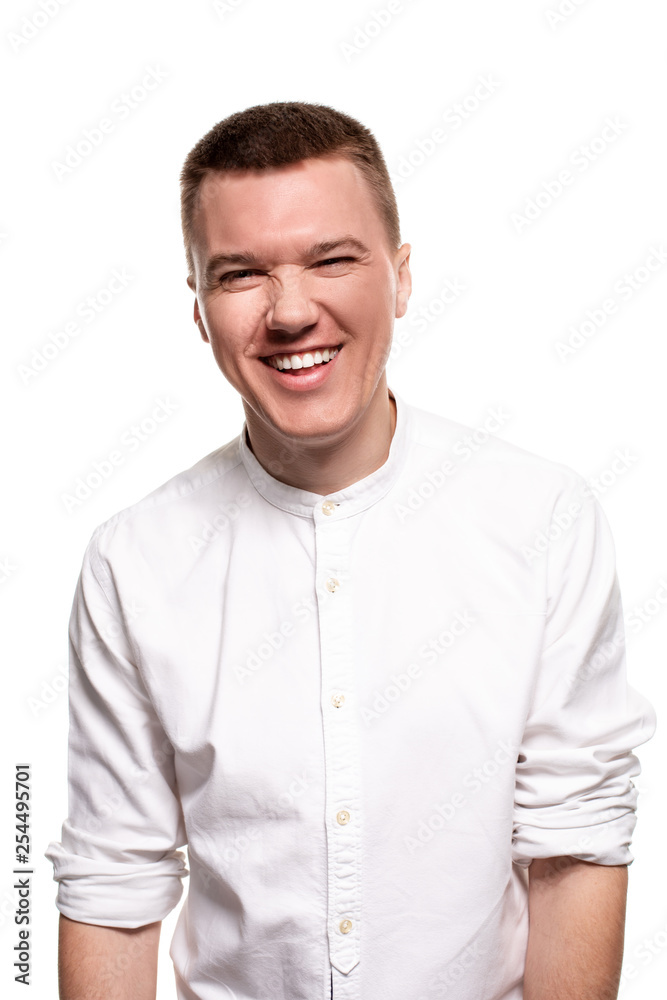 Charming handsome young man in a white shirt is making faces, while standing isolated on a white background Charming handsome young man in a white shirt is making faces, while standing isolated on a white background