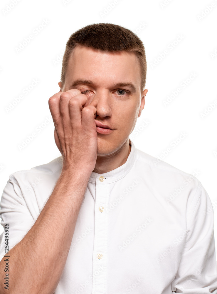 Charming handsome young man in a white shirt is making faces, while standing isolated on a white background