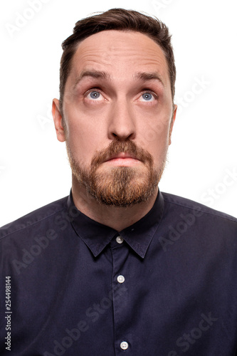 Portrait of a handsome, unshaven man, dressed in a dark blue shirt, standing against a white background. Self confident man.